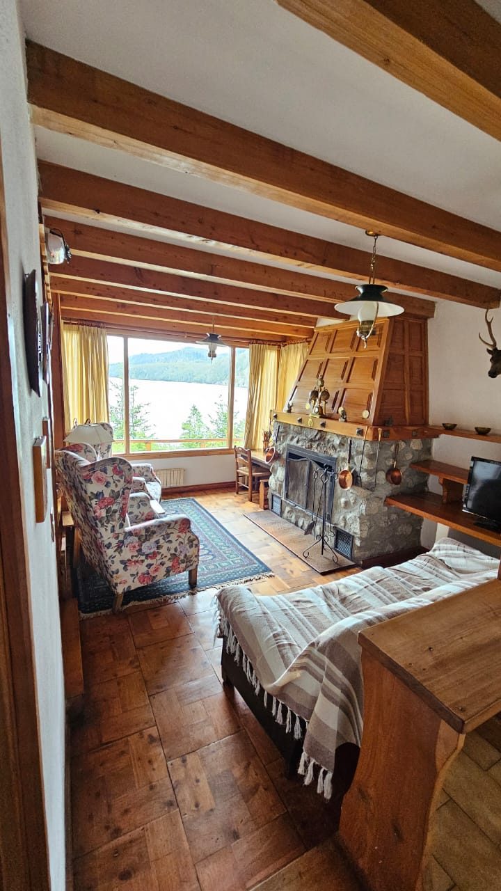 Living del hotel con hogar de piedra y ventanal al lago